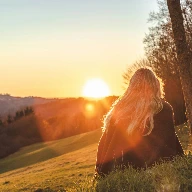 woman sitting on green grass looking at the sun