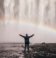 person in front of waterfalls with double rainbow during daytime
